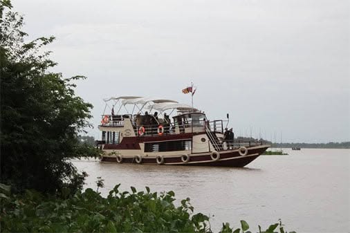 A multi-deck riverboat with a canopy-covered top deck cruising along a wide river in Cambodia during a Khmer Detours tour.
