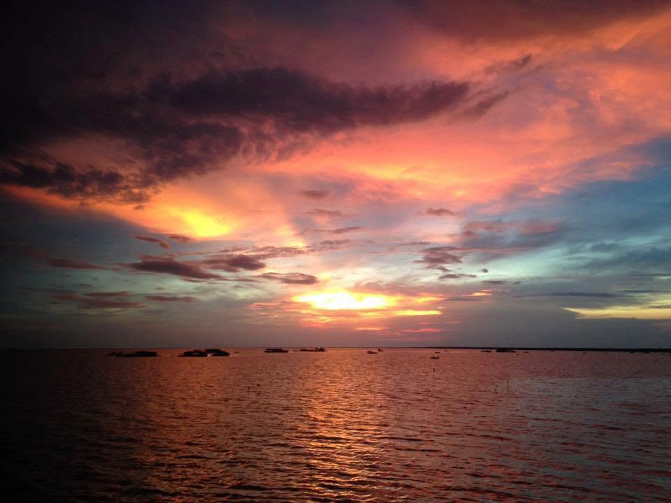 A dramatic pink and orange sunset sky with dark clouds breaking over the wide expanse of Tonle Sap Lake in Cambodia.